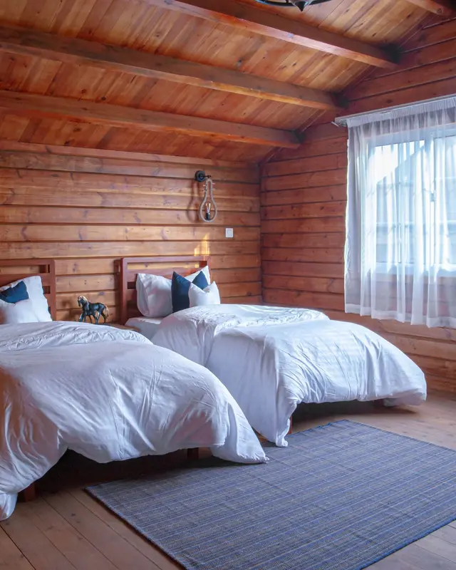 Quarto de madeira com duas camas de solteiro e janela com cortina branca
