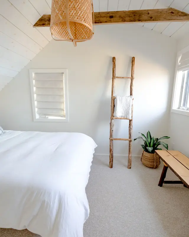Quarto branco de teto inclinado, com escada de madeira e luminária de palha
