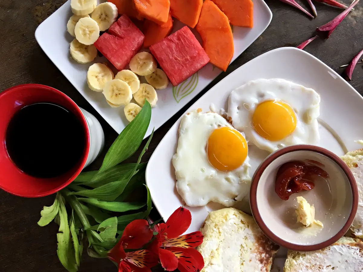 Mesa de café da manhã vista de cima, com frutas cortadas, ovos fritos e café