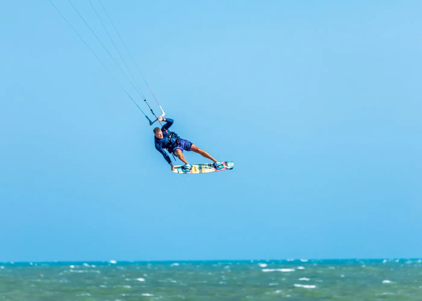 Kitesurfista no ar, contra o céu azul, sobre o mar