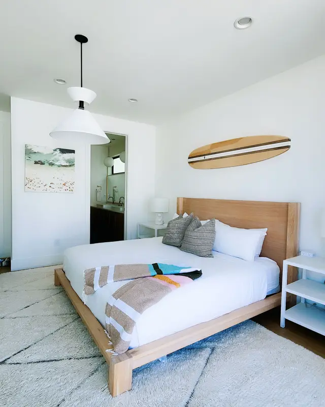 Quarto claro com cama de casal, tapete branco e uma prancha na parede