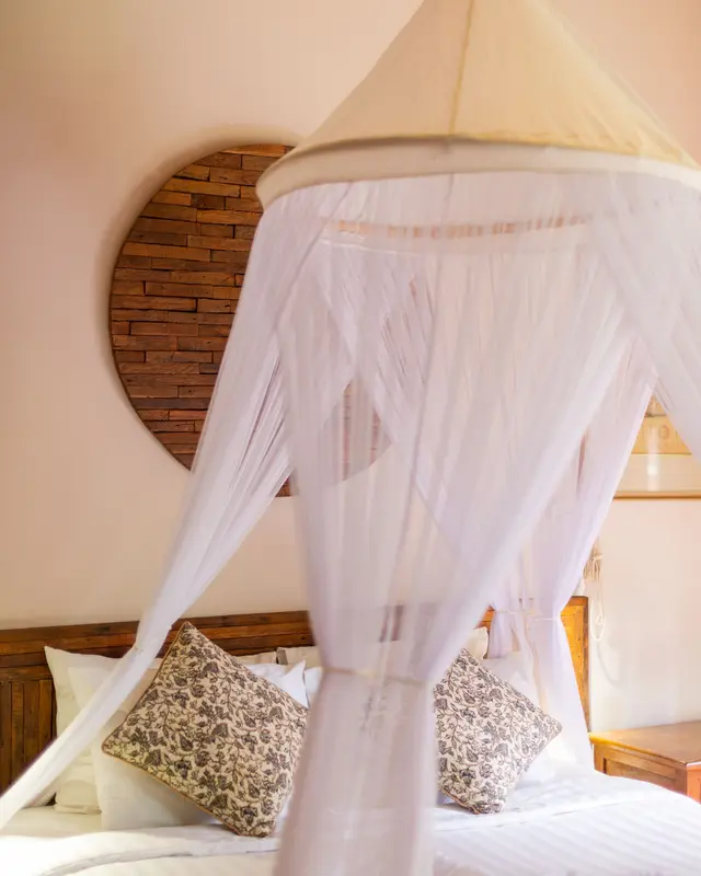 Cama de casal com mosquiteiro branco preso no teto e almofadas estampadas