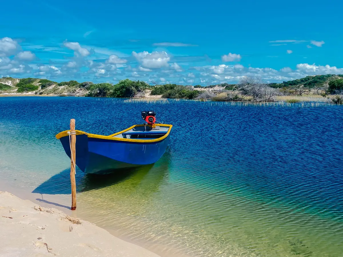 Barco de pesca azul ancorado em água rasa e transparente, perto da areia