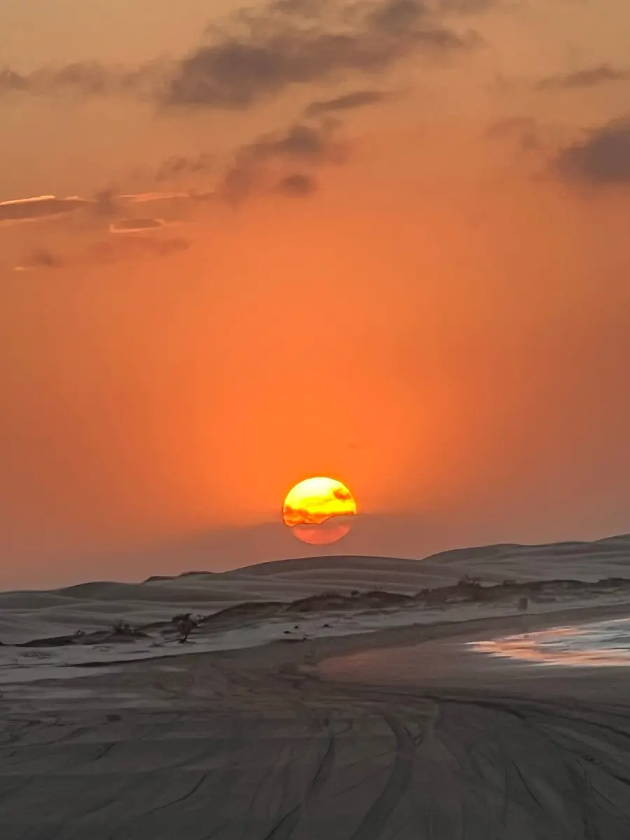 Sol laranja se pondo sobre dunas, com o céu alaranjado